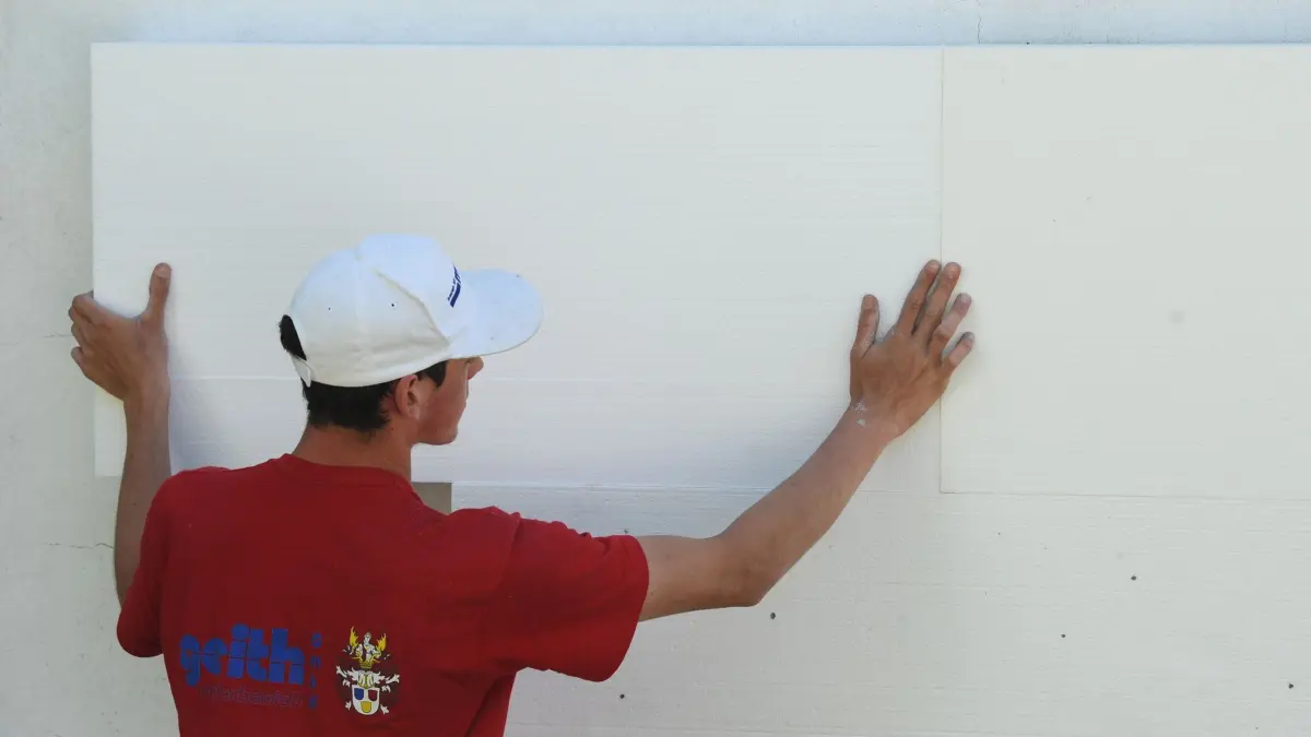 Wärmedämmung: ARCHIV - 07.07.2010, Bayern, Straubing: 07.07.2010, Bayern, Straubing: Ein Handwerker montiert eine Styroporplatte zur Wärmedämmung an die Fassade eines Kindergartens. (zu dpa: «Wärmedämmung und Balkone: Neues Recht in Kraft») Foto: Armin Weigel/dpa +++ dpa-Bildfunk +++