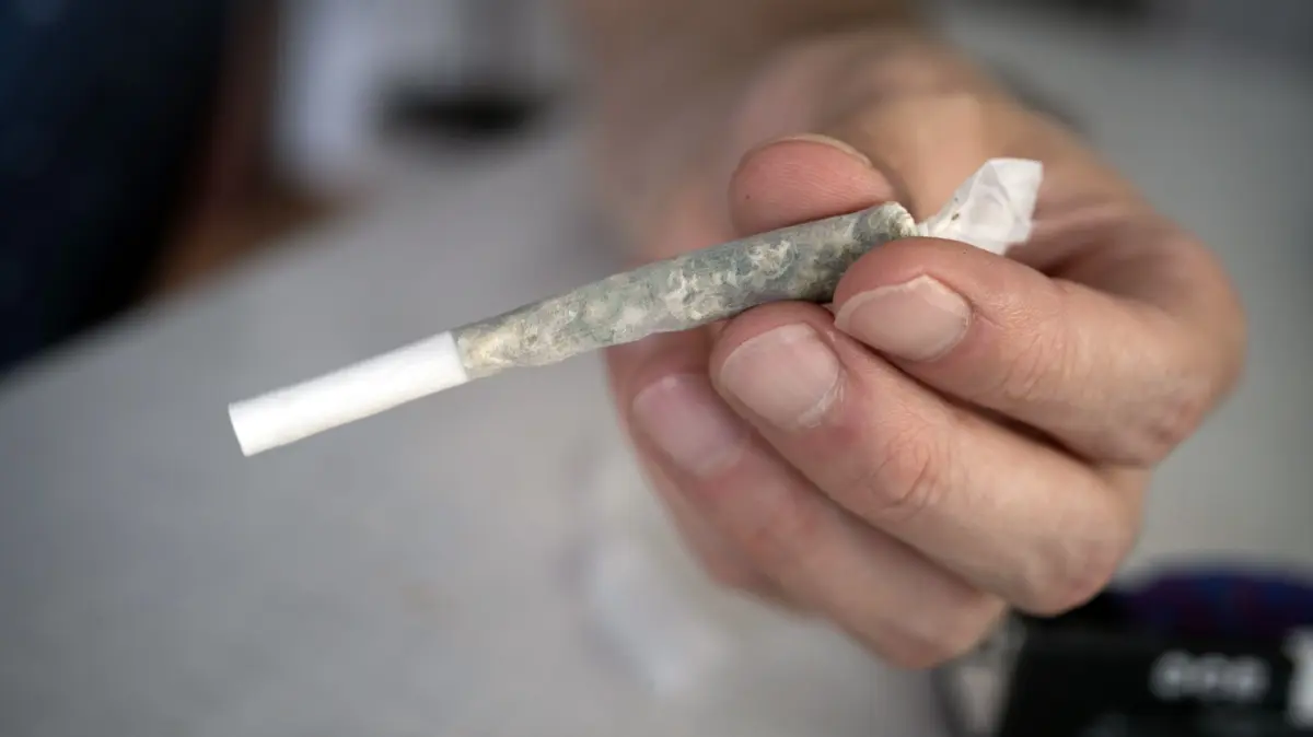 Diakonie-Chef Lenke fordert mehr Praevention gegen Cannabis-Sucht: Eine Hand haelt einen Cannabis - Joint in Offenbach, Hessen (Foto vom 21.07.2024). Der Chef der Diakonie in Niedersachsen, Hans-Joachim Lenke, fordert mehr Praevention gegen die Cannabis-Sucht. Anderthalb Jahre nach der Teillegalisierung der Droge wendeten sich mehr Menschen an die Suchtberatungsstellen der Diakonie, sagte Lenke im Gespraech mit dem Evangelischen Pressedienst (epd). Dort berichteten sie, dass durch die Legalisierung der Konsum in der Oeffentlichkeit zugenommen habe und dass der im Alltag haeufig wahrnehmbare typische Cannabis-Geruch fuer viele ein Trigger sei: "Das erschwert fuer viele die Abstinenz." Die Diakonie ist mit 35 Einrichtungen der groesste Traeger von Suchtberatungsstellen in Niedersachsen. (Siehe epd-Gespraech vom 30.12.2025) *** Local Caption *** 00510305