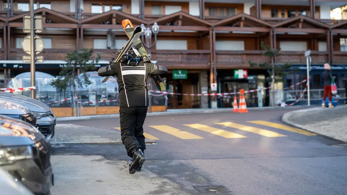 Explosion bei Silvesterparty in Skiort in der Schweiz: 01.01.2026, Schweiz, Crans-Montana: Ein Skifahrer läuft auf der Straße in der Nähe der Stelle, an der in der Bar und Lounge "Le Constellation" nach einer Explosion in den frühen Morgenstunden der Silvesternacht ein Feuer ausgebrochen ist. Bei einer Explosion und einem Brand in der Silvesternacht sind im noblen Schweizer Skiort Crans-Montana nach Polizeiangaben mehrere Menschen ums Leben gekommen. Foto: Alessandro Della Valle/KEYSTONE/dpa +++ dpa-Bildfunk +++