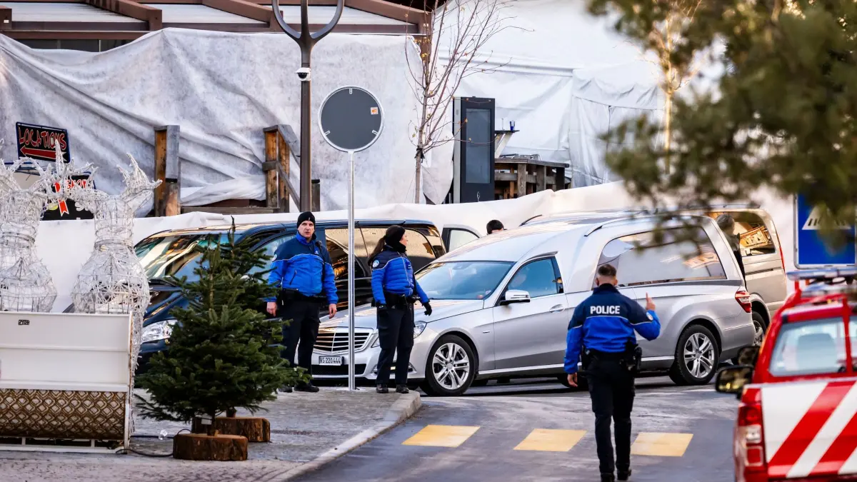 Tote bei Silvesterparty in Crans-Montana: 01.01.2026, Schweiz, Crans-Montana: Ein Leichenwagen fährt vor, während Polizeibeamte den Bereich inspizieren, in dem während der Silvesterfeierlichkeiten ein Feuer unbekannter Ursache in der Bar und Lounge «Le Constellation» ausbrach, bei dem es Tote und Verletzte gab. Foto: Jean-Christophe Bott/KEYSTONE/dpa +++ dpa-Bildfunk +++