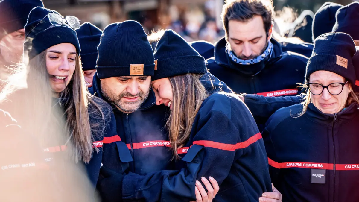 Firefighters from the Municipality of Crans-Montana react as they gather around a makeshift memorial to pay their respects by laying flowers, candles and messages near the Constellation bar, on January 4, 2026, in Crans-Montana in honour of the victims of the fire that ripped through the venue in the luxury Alpine ski resort on New Year's Eve. Authorities investigating the New Year's blaze in the Swiss resort of Crans-Montana have identified 24 of the 40 people killed, including 11 minors and six foreign nationals, police said on January 4, 2026. Also 119 were injured during the fire, most of them seriously, according to the latest toll. (Photo by MAXIME SCHMID / AFP)