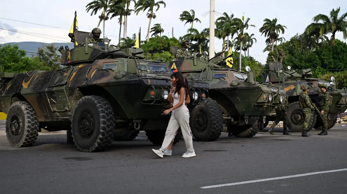 A woman walks past military vehicles at the border crossing with Venezuela in Cucuta, Colombia, on January 3, 2026, after US forces captured Venezuela's President Nicolas Maduro. President Donald Trump said on January 3, 2026, that US forces had captured Venezuela's leader Nicolas Maduro after bombing the capital Caracas and other cities in a dramatic climax to a months-long standoff between Trump and his Venezuelan arch-foe. (Photo by Raul ARBOLEDA / AFP)