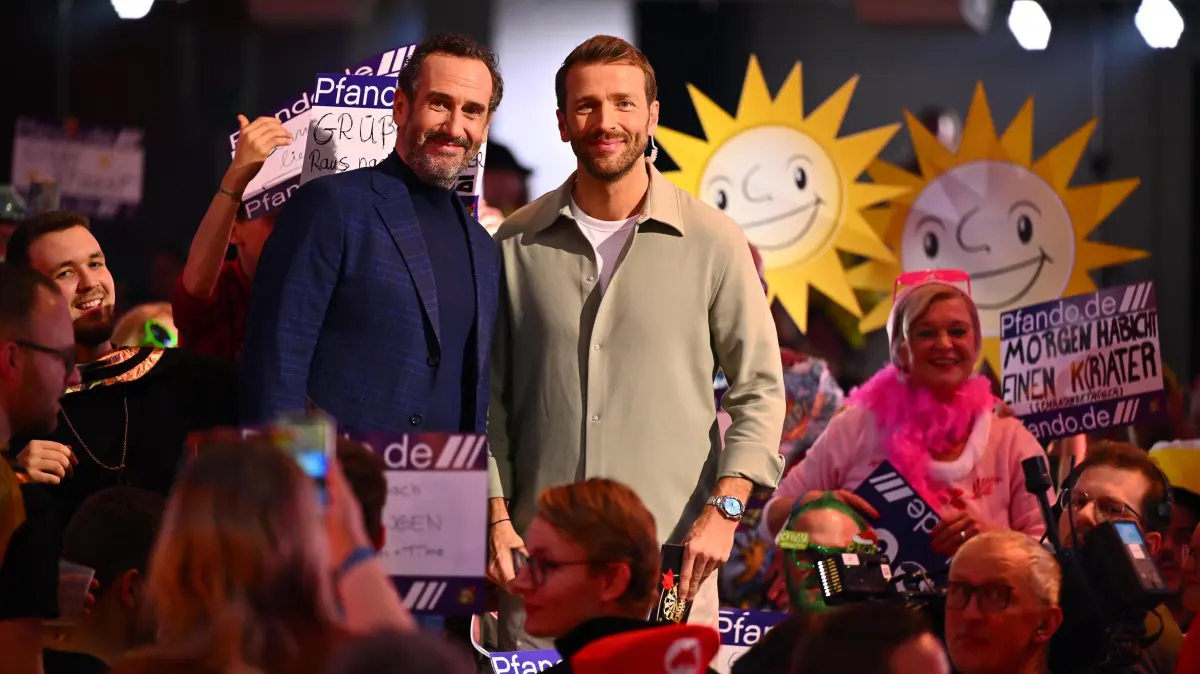 Christian Düren (r.) moderiert „Die Promi-Darts-WM“ 2026, während Elmar Paulke kommentiert.