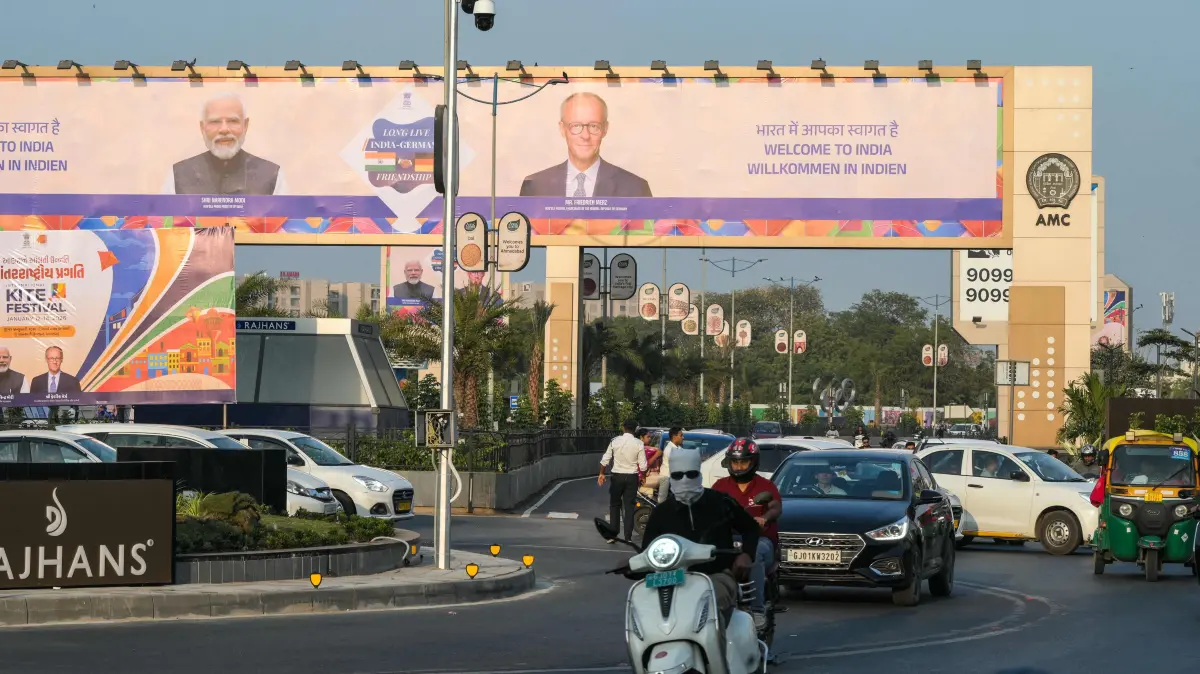 Commuters ride past a billboard featuring India's Prime Minister Narendra Modi (L) and German Chancellor Friedrich Merz ahead of their visit, along a street in Ahmedabad on January 10, 2026. (Photo by Shammi MEHRA / AFP)