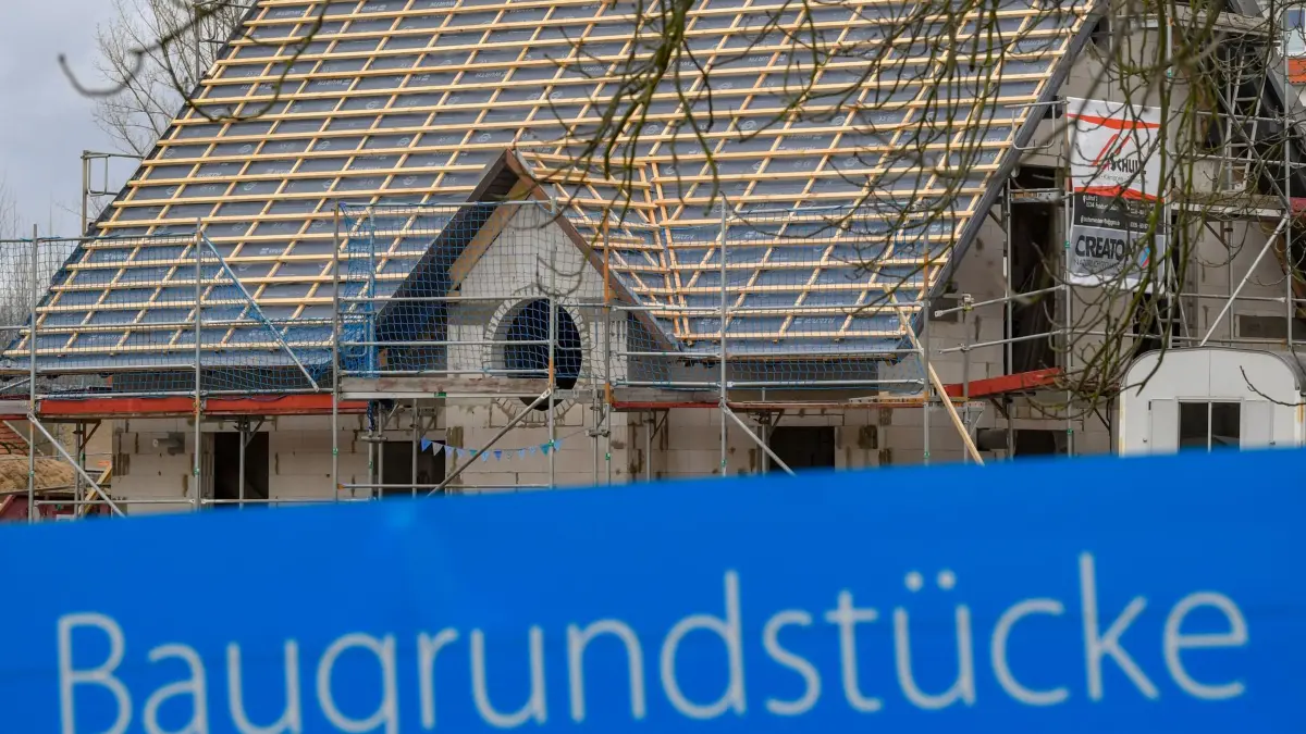 Grüne wollen Erwerb des Eigenheims erleichtern: ARCHIV - 10.01.2019, Brandenburg, Frankfurt (Oder): Ein Schild mit der Aufschrift «Baugrundstücke» steht am Rande eines Baufeldes mit einem Rohbau eines Eigenheimes. (zu dpa: «Bayerns Grüne wollen Traum vom Eigenheim wiederbeleben») Foto: Patrick Pleul/dpa-Zentralbild/dpa +++ dpa-Bildfunk +++