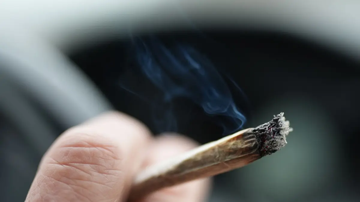 Cannabis im Straßenverkehr: PRODUKTION - 05.01.2025, Hamburg: ILLUSTRATION - Ein Mann raucht während der Autofahrt am Steuer einen Joint. (zu dpa: «Illegale Geschäfte bei Verkehrskontrolle aufgedeckt») Foto: Marcus Brandt/dpa +++ dpa-Bildfunk +++