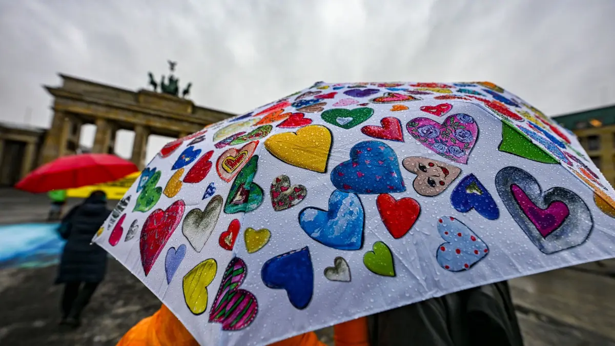 Regenwetter in Berlin: 14.01.2026, Berlin: Passanten stehen bei regnerischem Wetter mit einem bunten Regenschirm auf dem Pariser Platz vor dem Brandenburger Tor. Foto: Jens Kalaene/dpa +++ dpa-Bildfunk +++