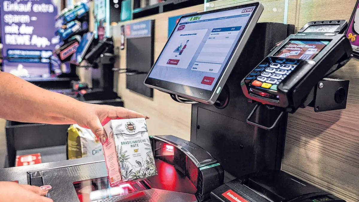 Eine Frau scannt in einer Rewe-Fliale ein Produkt an einer Selbstbedienungskasse. (zu dpa: «SB-Kassen boomen – warum sie trotzdem nicht jeder mag»)