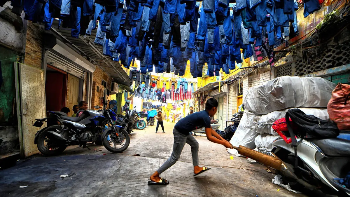 Blue Jeans Lane in Kolkata: 17.01.2026, Indien, Kolkata: Kinder spielen Kricket in den Straßen eines Slums unter gebrauchten Jeanshosen, die auf dem Secondhand-Markt verkauft werden. Der «Jeans Gully», wie er gemeinhin genannt wird, ist eine besondere Gegend in Kolkata, in der ausrangierte, übersehene und unverkaufte Jeans und Latzhosen aus der ganzen Stadt zusammenkommen und eine neue Bestimmung finden. Foto: Avishek Das/SOPA Images via ZUMA Press Wire/dpa +++ dpa-Bildfunk +++