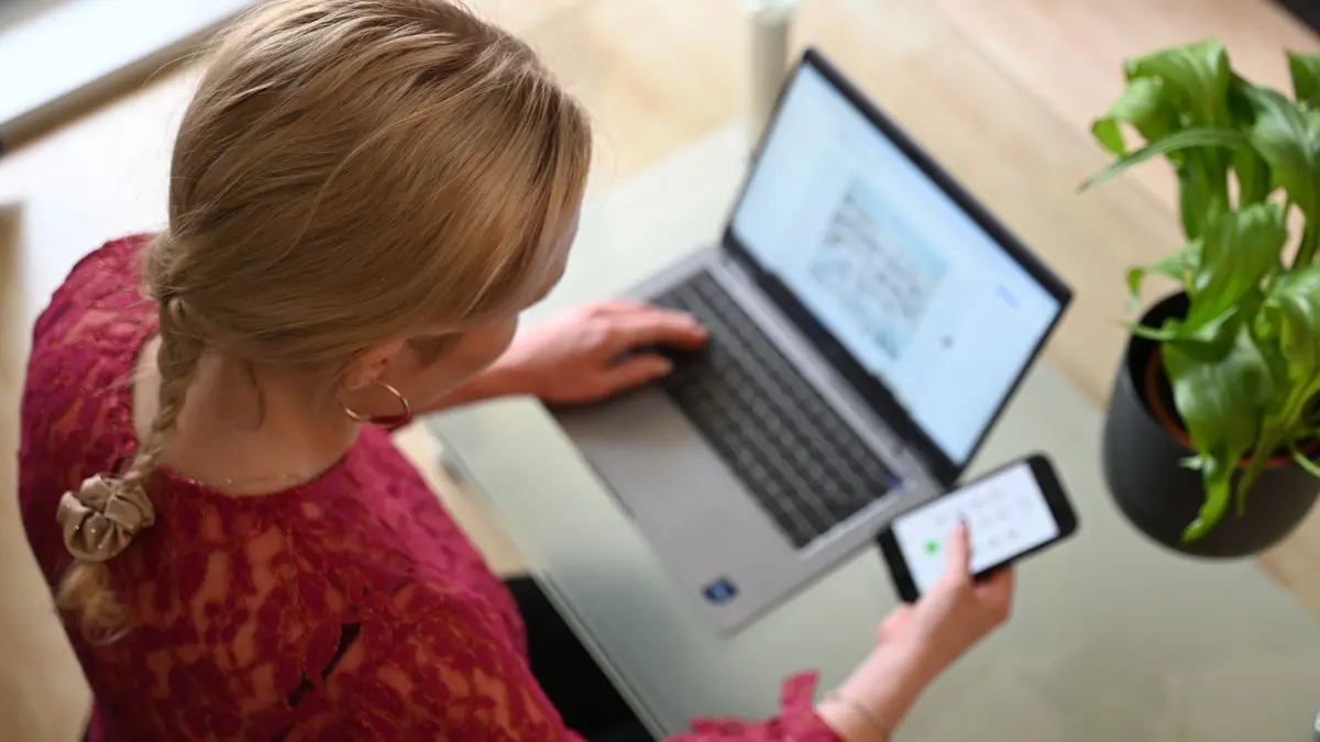 Hausärzte für schärfere Regeln bei Online-Krankschreibungen: SYMBOLBILD - 03.07.2024, Berlin: Eine Frau sitzt zuhause an einem Glastisch und tippt auf einem Laptop, in der rechten Hand hält sie ein Smartphone. Angesichts der Debatte um die Krankentage deutscher Arbeitnehmer fordert der Hausärztinnen- und Hausärzteverband schärfere Regeln für Online-Krankschreibungen. (zu dpa: «Hausärzte für schärfere Regeln bei Online-Krankschreibungen») Foto: Helena Dolderer/dpa +++ dpa-Bildfunk +++