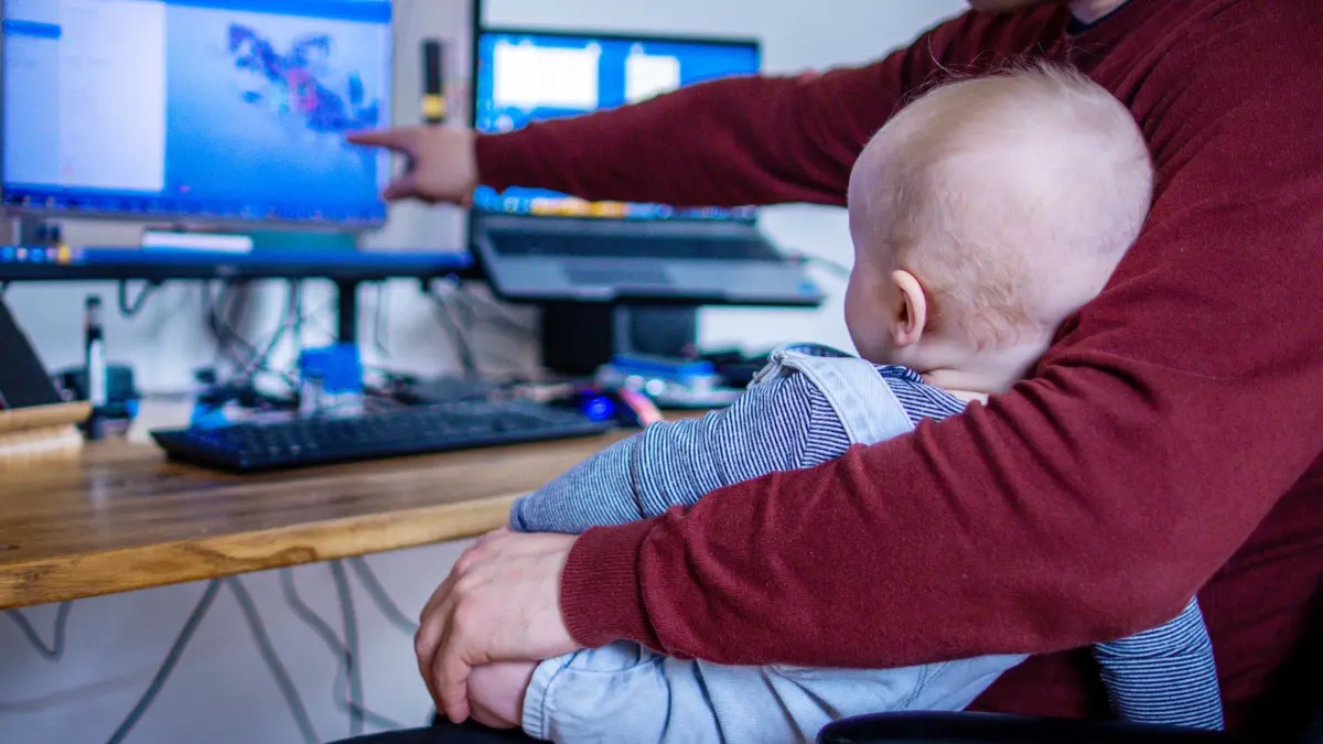 Illustration - Vater im Homeoffice: ARCHIV - 10.05.2023, Schleswig-Holstein, Groß Grönau: Ein junger Vater arbeitet im Home-Office mit seinem sechs Monate alten Sohn im Arbeitszimmer. (RECROP) (zu dpa: «Niedersächsische Mütter arbeiten meist in Teilzeit») Foto: Jens Büttner/dpa +++ dpa-Bildfunk +++