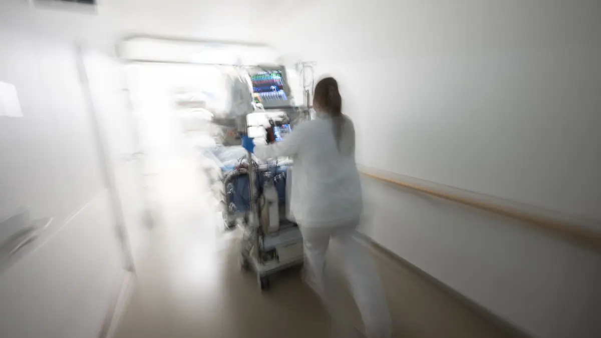 Pflegerin fährt eine Intensivpatientin durch denGang einer Klinik