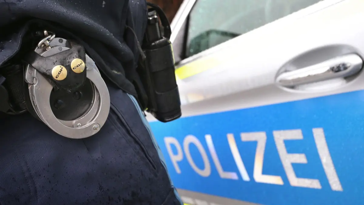 ARCHIV - 15.03.2019, Bayern, Kempten: ILLUSTRATION - Ein Polizist mit Handschellen und einer Pistole am Gürtel steht vor einem Streifenwagen. (zu dpa: «Dutzende Hühner in Bauwagen entdeckt - Diebstahl?») Foto: Karl-Josef Hildenbrand/dpa +++ dpa-Bildfunk +++