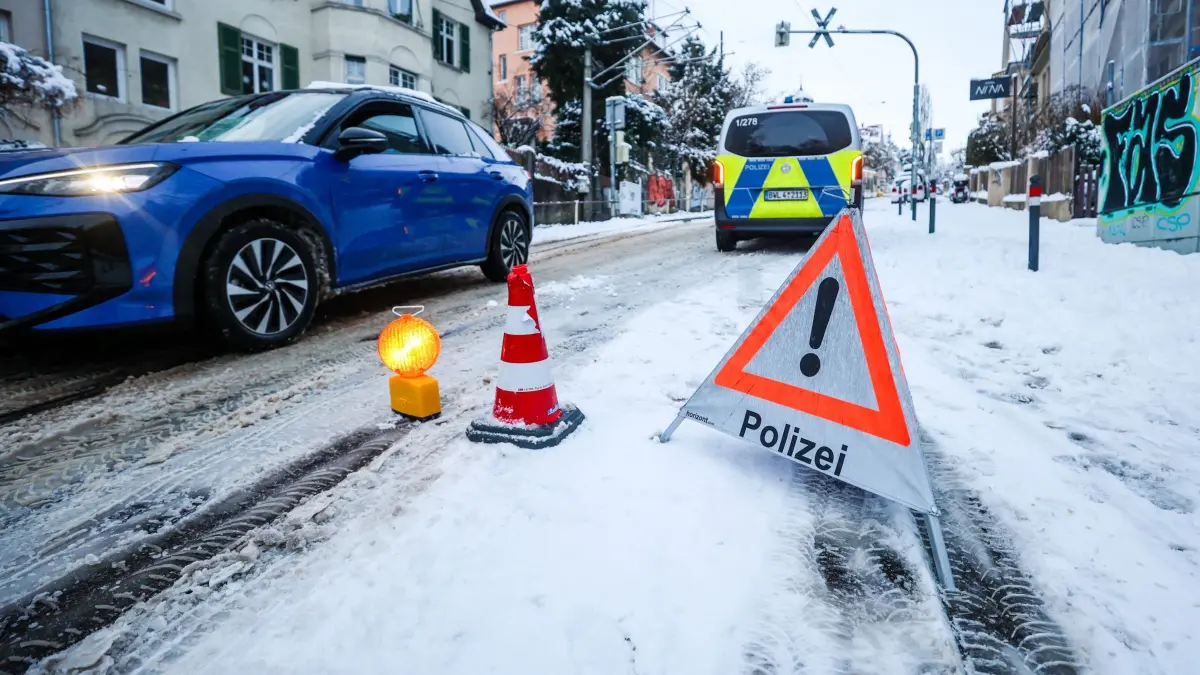 Winterwetter in Stuttgart: 26.01.2026, Baden-Württemberg, Stuttgart: Die Polizei weist Autofahrer auf eine Gefahrenstelle an einer schneebedeckten Straße hin, die an einem Hang liegt. In der Nacht hatte es in der Region Stuttgart starken Schneefall gegeben. Foto: Christoph Schmidt/dpa +++ dpa-Bildfunk +++