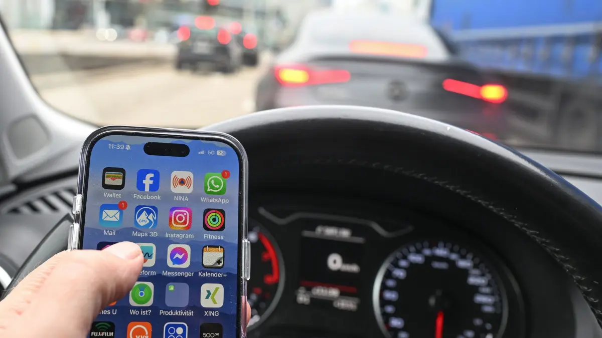 Eine Hand hält in einem Auto am Steuer ein Handy: ILLUSTRATION - Ein kurzer Blick aufs Handy kann reichen, um alles andere zu übersehen. Am besten Handy komplett außer Sicht und Reichweite. (zu dpa: «Mit diesen Tipps minimieren Sie Ablenkung am Steuer») Foto: Bernd Weißbrod/dpa/dpa-tmn - Honorarfrei nur für Bezieher des dpa-Themendienstes +++ dpa-Themendienst +++