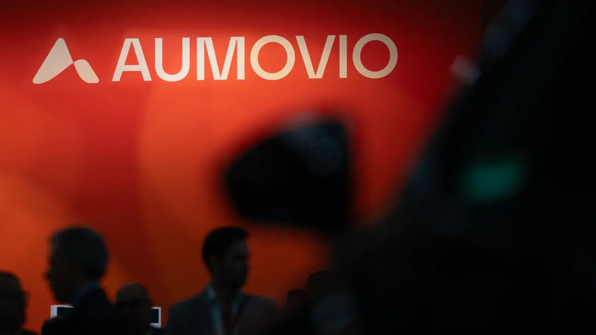 Aumovio: ARCHIV - 10.09.2025, Bayern, München: Das Logo von Aumovio SE ist während der Internationalen Automobil-Ausstellung (IAA Mobility) zu sehen. Im Vordergrund laufen Messebesucher. (zu dpa: «Hier will ein großer Zulieferer im Südwesten Stellen abbauen») Foto: Leonie Asendorpf/dpa +++ dpa-Bildfunk +++