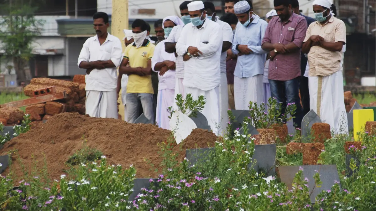 24.05.2018, Indien, Kozhikode: Angehörige und Freunde tragen Schutzmasken und beten nach der Beerdigung eines Opfers, das aufgrund des Nipah-Virus verstarb. Beim Ausbruch des gefährlichen Nipah-Virus in Indien sind mehrere Menschen gestorben. Der Erreger kann bei Menschen Fieber, Atemwegserkrankungen und tödliche Hirnhautentzündungen verursachen. Es gibt weder eine Impfung noch eine wirkungsvolle Behandlung. Foto: K.Shijith/AP/dpa +++ dpa-Bildfunk +++