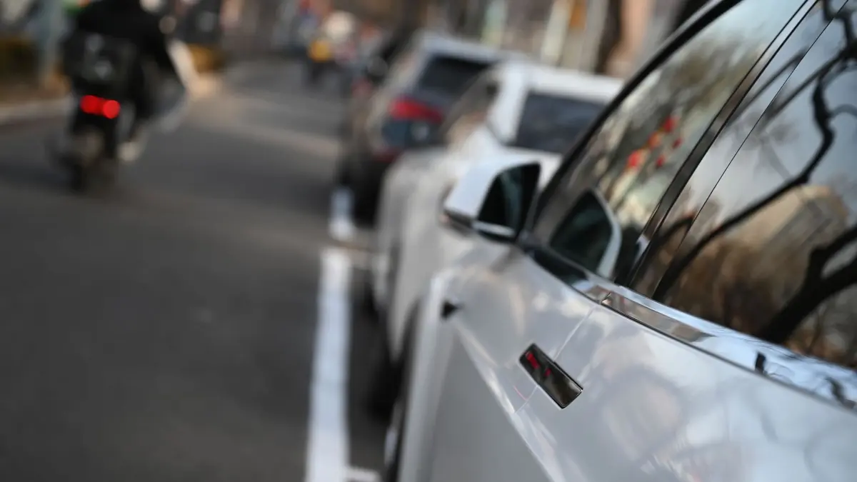 Versenkbarer Auto-Türgriff: 03.02.2026, China, Peking: Menschen fahren an einem Elektroauto vorbei, an dem ein versenkbarer Türgriff angebracht ist. China hat einen neuen Standard für versenkbarer Türgriffe veröffentlicht, die ab kommendem Jahr verboten sein sollen. Foto: Johannes Neudecker/dpa +++ dpa-Bildfunk +++