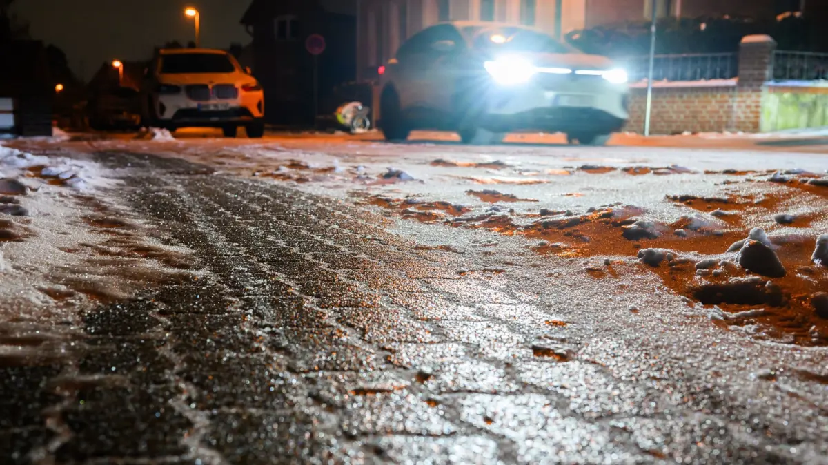 Glatteis in Niedersachsen: 04.02.2026, Niedersachsen, Laatzen: Eine spiegelglatte Eisschicht glänzt auf einem Gehweg und Straße in der Region Hannover. Schnee und regional in der Folge gefrierender Regen haben in der Nacht für glatte Straßen gesorgt. Foto: Julian Stratenschulte/dpa +++ dpa-Bildfunk +++