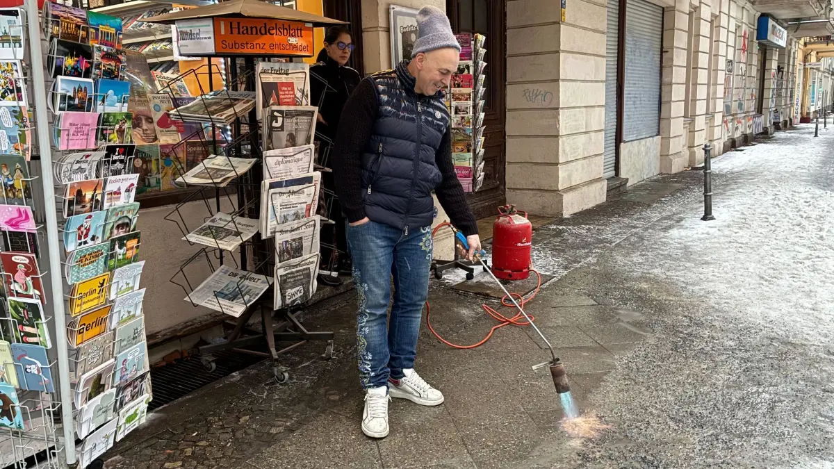 Winter in Berlin: 06.02.2026, Berlin: In Kreuzberg beseitigt ein Kioskbesitzer das festsitzende Glatteis vor seinem Geschäft mit einem Dachpappenbrenner. Foto: Caroline Bock/dpa - ACHTUNG: Nur zur redaktionellen Verwendung im Zusammenhang mit der aktuellen Berichterstattung und nur mit vollständiger Nennung des vorstehenden Credits +++ dpa-Bildfunk +++