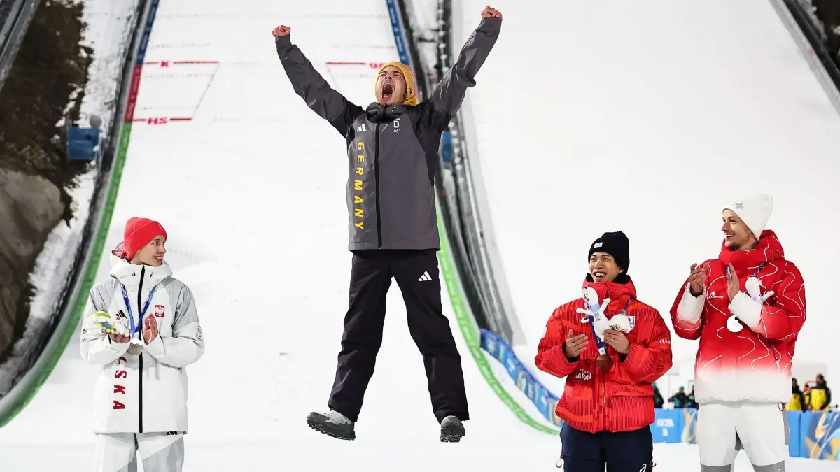 Olympische Winterspiele 2026: 09.02.2026, Italien, Predazzo: Olympia, Olympische Winterspiele Mailand Cortina 2026, Ski nordisch/Skispringen, Normalschanze, Männer, Durchgang 2, Olympiasieger Philipp Raimund (M, Deutschland) jubelt neben dem Zweitplatzierten Kacper Tomasiak (l, Polen) und den beiden Drittplatzierten Ren Nikaido (2.v.r, Japan) und Gregor Deschwanden (Schweiz) bei der Siegerehrung über seine Goldmedaille. Foto: Daniel Karmann/dpa +++ dpa-Bildfunk +++