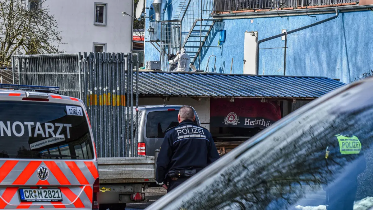 Frau stirbt nach Schüssen: 10.02.2026, Baden-Württemberg, Schrozberg: Polizisten in Spezialanzügen (hinten) stehen bei der Spurensicherung an der Rückseite eines Wohn- und Geschäftshauses, an dem ein Mann seine Frau erschossen haben soll. Wie die Polizei mitteilte, gab der Mann mehrere Schüsse auf die Frau ab. Der Mann konnte wenig später von der Polizei festgenommen werden. Foto: Fabian Koss/onw-images/dpa - ACHTUNG: Ein Kennzeichen wurde aus rechtlichen Gründen gepixelt +++ dpa-Bildfunk +++