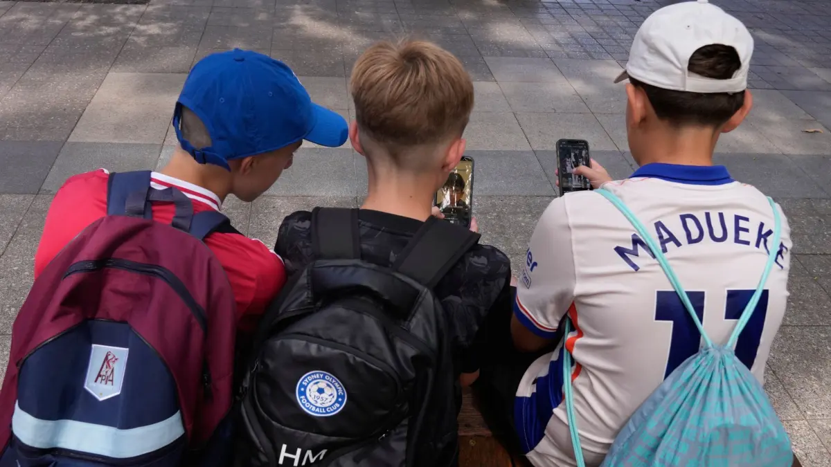 Diskussion um Social-Media-Verbot für Schüler: 08.12.2025, Australien, Sydney: Drei Elfjährige benutzen ihre Telefone, während sie vor einer Schule in Sydney sitzen. In Australien dürfen Kinder und Jugendliche unter 16 Jahren seit zwei Monaten keine eigenen Konten mehr auf vielen großen Social-Media-Plattformen besitzen. Ein Verbot wird auch in Deutschland kontrovers diskuttiert. (zu dpa: «Social-Media-Verbot für unter 16-Jährige? Parteien uneins») Foto: Rick Rycroft/AP/dpa +++ dpa-Bildfunk +++