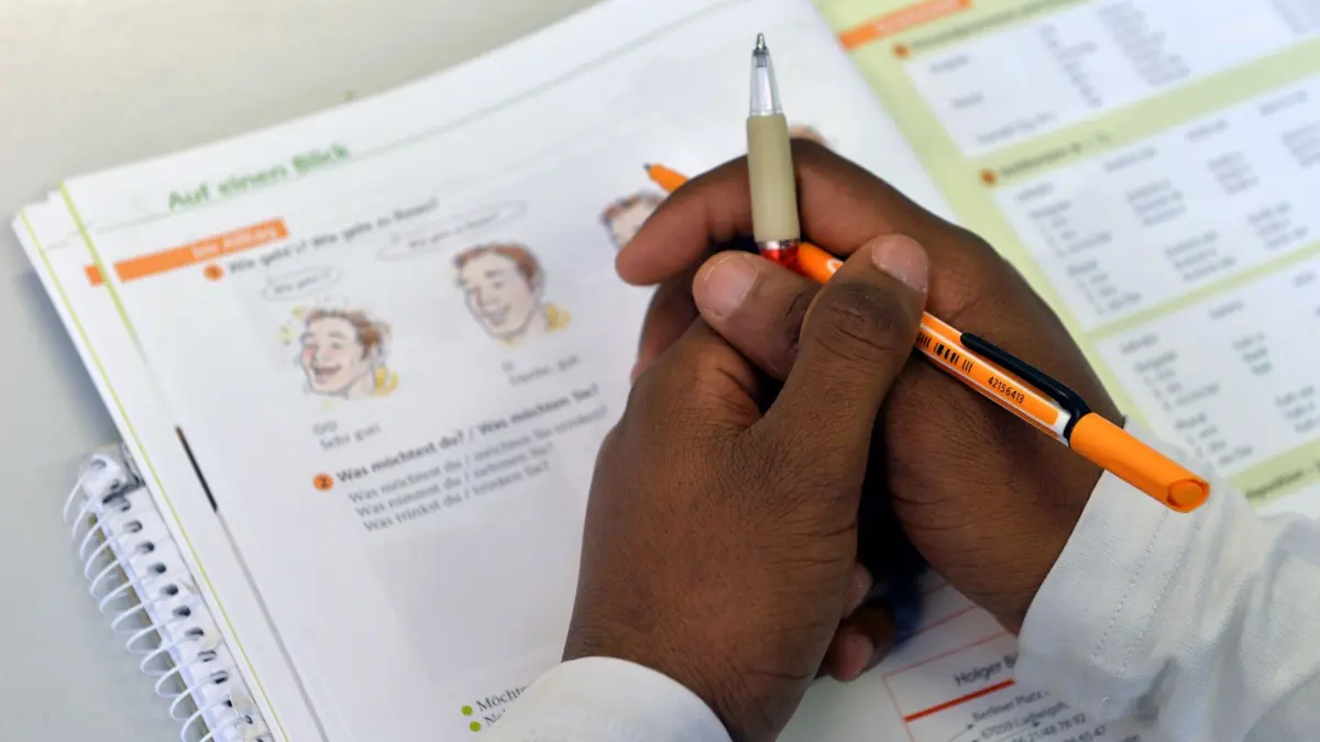 Deutschkurse für Flüchtlinge: ARCHIV - 11.11.2015, Sachsen-Anhalt, Halle (Saale): ILLUSTRATION - Ein Lehrbuch liegt in einem Deutschkurs für Flüchtlinge vor einem jungen Mann auf der Schulbank. Die FDP in der Hamburgischen Bürgerschaft fordert eine Verbesserung der Sprachkurse für Flüchtlinge. (zu dpa: «Hamburg kritisiert Kürzungen bei Sprachkursen») Foto: Hendrik Schmidt/dpa-Zentralbild/dpa +++ dpa-Bildfunk +++