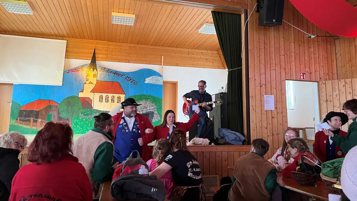 Der Ortsvorsteher Johannes Metzner (an der Gitarre) lässt die Narren sein selbst gedichtetes Rohrdorf-Lied singen. Bianca Fuhrer (rechts vor der Bühne) und Alexander Michel (links vor der Bühne) meistern das sogar hopsend.