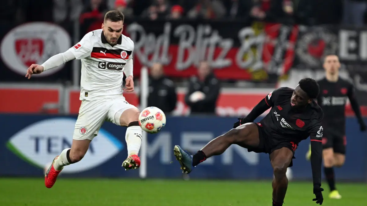 Bayer Leverkusen - FC St. Pauli: 14.02.2026, Nordrhein-Westfalen, Leverkusen: Fußball: Bundesliga, Bayer Leverkusen - FC St. Pauli, 22. Spieltag, BayArena. Ernest Poku (Bayer Leverkusen) und James Sands (FC St. Pauli, l) kämpfen um den Ball. Foto: Federico Gambarini/dpa - WICHTIGER HINWEIS: Gemäß den Vorgaben der DFL Deutsche Fußball Liga bzw. des DFB Deutscher Fußball-Bund ist es untersagt, in dem Stadion und/oder vom Spiel angefertigte Fotoaufnahmen in Form von Sequenzbildern und/oder videoähnlichen Fotostrecken zu verwerten bzw. verwerten zu lassen. +++ dpa-Bildfunk +++