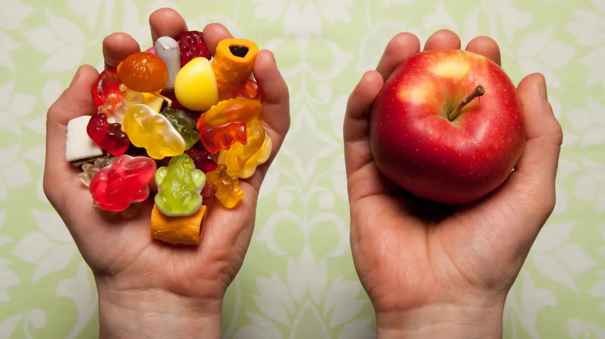 Kurz erklaert: Warum fasten Menschen?: Symbolfoto zum Thema Fasten: Eine Hand ist voller Suessigkeiten, die andere Hand haelt einen Apfel. Tagsueber nicht essen, sieben Wochen auf Alkohol verzichten, jeden Tag Naehe zu Gott suchen: Menschen fasten auf ganz unterschiedliche Weise. "Fasten gab und gibt es in fast allen Kulturen und Religionen. Es hat einen inneren, tieferen Sinn, der vielen Menschen guttut", sagt der evangelische Theologe Wolfgang Reinbold. Die Gruende dafuer seien ebenso verschieden wie die Formen des Fastens. "Es geht um Askese, Kontrolle, Verzicht, Reinigung, Trauer, Busse und vieles andere mehr, heute nicht zuletzt auch um Gesundheit. Einen einheitlichen Sinn gibt es nicht." (Siehe epd-Hintergrund vom 15.02.2026)
