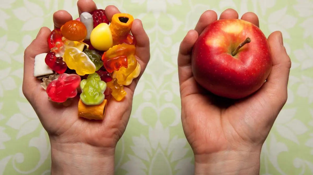 Kurz erklaert: Warum fasten Menschen?: Symbolfoto zum Thema Fasten: Eine Hand ist voller Suessigkeiten, die andere Hand haelt einen Apfel. Tagsueber nicht essen, sieben Wochen auf Alkohol verzichten, jeden Tag Naehe zu Gott suchen: Menschen fasten auf ganz unterschiedliche Weise. "Fasten gab und gibt es in fast allen Kulturen und Religionen. Es hat einen inneren, tieferen Sinn, der vielen Menschen guttut", sagt der evangelische Theologe Wolfgang Reinbold. Die Gruende dafuer seien ebenso verschieden wie die Formen des Fastens. "Es geht um Askese, Kontrolle, Verzicht, Reinigung, Trauer, Busse und vieles andere mehr, heute nicht zuletzt auch um Gesundheit. Einen einheitlichen Sinn gibt es nicht." (Siehe epd-Hintergrund vom 15.02.2026)