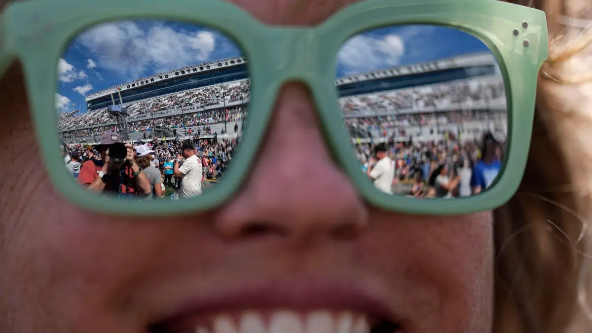 Nascar Daytona 500 Autorennen: 15.02.2026, USA, Daytona Beach: Kylie Givens steht vor dem NASCAR Daytona 500 Autorennen auf dem Daytona International Speedway auf der Strecke, während sich die Umgebung in den Gläsern ihrer Sonnenbrille spiegelt. Foto: Mike Stewart/AP/dpa +++ dpa-Bildfunk +++