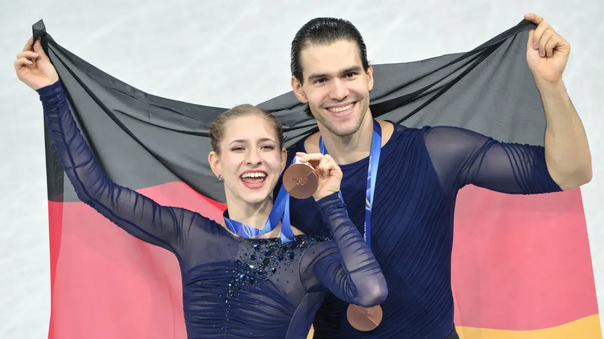 Olympische Winterspiele 2026: 17.02.2026, Italien, Mailand: Olympia, Olympische Winterspiele Mailand Cortina 2026, Eiskunstlauf, Paarlauf, Kür, Minerva Hase und Nikita Volodin aus Deutschland freuen sich mit der Landesfahne über die Bronzemedaille. Foto: Peter Kneffel/dpa +++ dpa-Bildfunk +++
