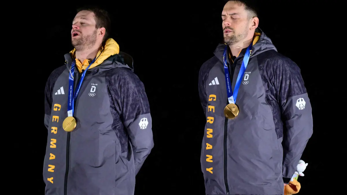 Gold medallists Germany's Johannes Lochner (L) and Germany's Georg Fleischhauer listen to the national anthem on the podium after competing in the bobsleigh men's 2-man event at Cortina Sliding Centre during the Milano Cortina 2026 Winter Olympic Games in Cortina d'Ampezzo on February 17, 2026. (Photo by Stefano RELLANDINI / AFP)