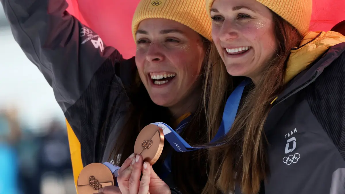 776396186: Bronze medallists Germany's Coletta Rydzek (L) and Germany's Laura Gimmler celebrate on the podium of the women's team cross country free sprint final event of the Milano Cortina 2026 Winter Olympic Games at Tesero Cross-Country Skiing Stadium in Lago di Tesero (Val di Fiemme), on February 18, 2026. (Photo by Anne-Christine POUJOULAT / AFP)