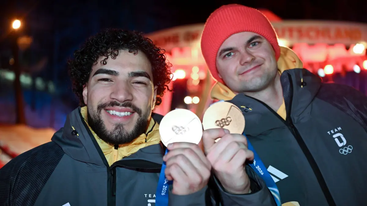 Olympische Winterspiele 2026: 18.02.2026, Italien, Cortina D'ampezzo: Olympia, Olympische Winterspiele Mailand Cortina 2026, Deutsches Haus, die Bob-Fahrer Adam Ammour (l) und Alexander Schaller (beide Deutschland) zeigen ihre Bronzemedaillen im Zweierbob. Foto: Robert Michael/dpa +++ dpa-Bildfunk +++