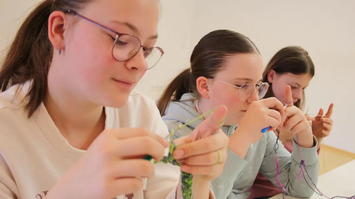 Lilly, Marla und Mara (von links) sind konzentriert bei der Arbeit. Während Lilly bereits einige Reihen gehäkelt hat, versuchen sich Marla und Mara noch an gleichmäßigen Luftmaschen.