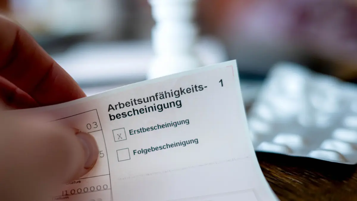 Eine Person hält eine Arbeitsunfähigkeitsbescheinigung: ILLUSTRATION - Eine Krankschreibung bleibt auch nach einer Kündigung wirksam, wenn sie medizinisch begründet ist. (zu dpa: «Krank nach Kündigung – Gericht schützt Lohnanspruch») Foto: Sina Schuldt/dpa - Honorarfrei nur für Bezieher des dpa-Themendienstes +++ dpa-Themendienst +++