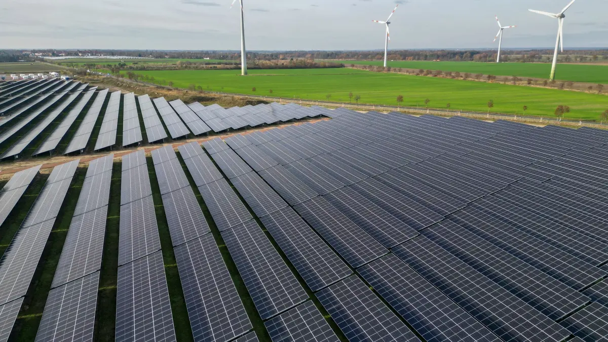 Windräder hinter Solarpark: ARCHIV - 12.11.2025, Sachsen-Anhalt, Zerbst: Windkraftanlagen drehen sich hinter den Solaranlagen eines neuen PV-Batteriespeicher-Hybridkraftwerks. (Luftaufnahme mit Drohne) (zu dpa: «Ökostrom: Was Reiches Netzpaket für Sachsen bedeutet») Foto: Jan Woitas/dpa +++ dpa-Bildfunk +++