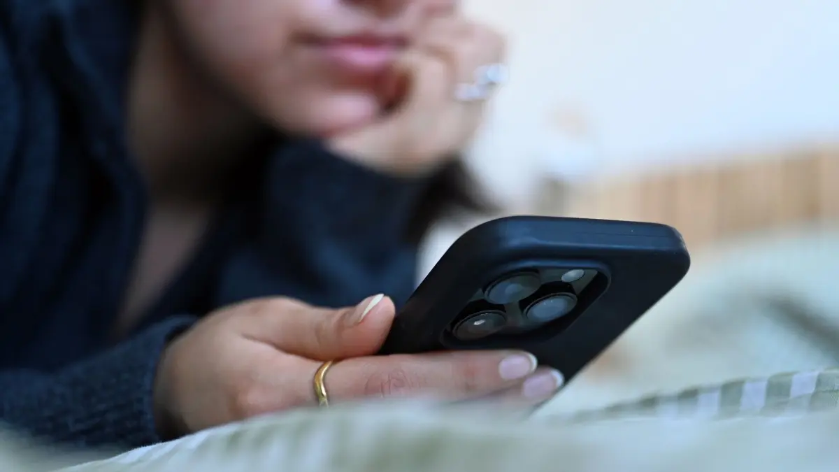 Frau liegt auf einem Bett und schaut auf ihr Smartphone: ILLUSTRATION - Eine App auf Rezept: Digitale Gesundheitsanwendungen können bei verschiedenen psychischen Krankheiten unterstützend eingesetzt werden. (zu dpa: «Psychische Gesundheit per App: Funktioniert das wirklich?») Foto: Elisa Schu/dpa/dpa-tmn - Honorarfrei nur für Bezieher des dpa-Themendienstes +++ dpa-Themendienst +++