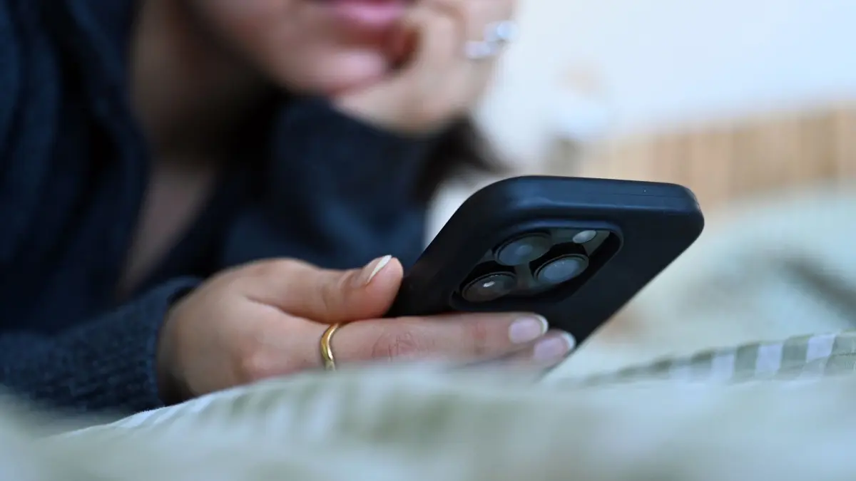 Frau liegt auf einem Bett und schaut auf ihr Smartphone: ILLUSTRATION - Eine App auf Rezept: Digitale Gesundheitsanwendungen können bei verschiedenen psychischen Krankheiten unterstützend eingesetzt werden. (zu dpa: «Psychische Gesundheit per App: Funktioniert das wirklich?») Foto: Elisa Schu/dpa/dpa-tmn - Honorarfrei nur für Bezieher des dpa-Themendienstes +++ dpa-Themendienst +++