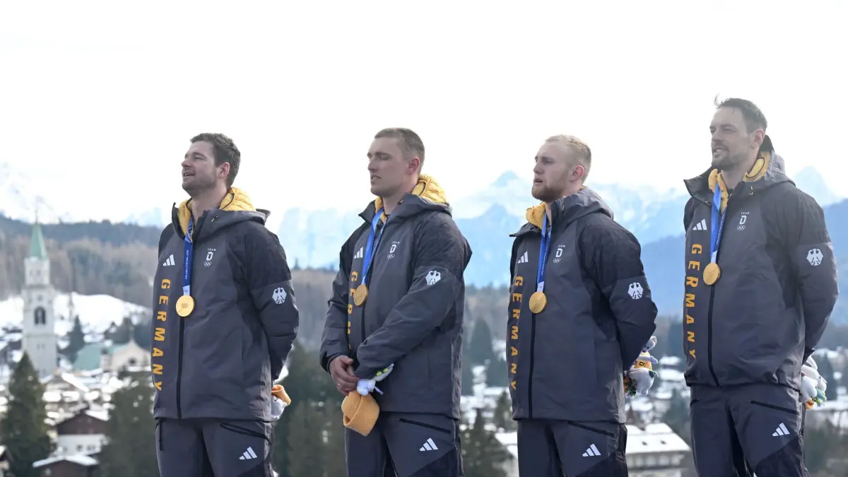 Olympische Winterspiele 2026: 22.02.2026, Italien, Cortina D'ampezzo: Olympia, Olympische Winterspiele Mailand Cortina 2026, Bob, Viererbob, Männer, Durchgang 4 im Cortina Sliding Centre, Johannes Lochner (Pilot, l-r), Thorsten Margis, Jörn Wenzel und Georg Fleischhauer (Deutschland) hören bei der Siegerehrung mit der Goldmedaille die Nationalhymne. Foto: Robert Michael/dpa +++ dpa-Bildfunk +++