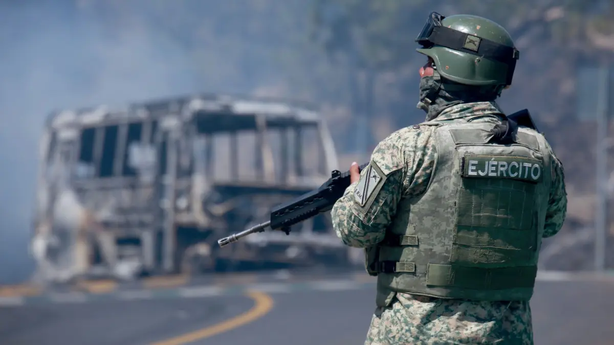 Drogenkrieg in Mexiko - Cointzio: 22.02.2026, Mexiko, Cointzio: Ein Soldat steht neben einem ausgebrannten Bus, das in Cointzio im mexikanischen Bundesstaat Michoacán, nach dem Tod des Anführers des Kartells der Neuen Generation von Jalisco, «El Mencho», in Brand gesetzt wurde. Foto: Armando Solis/AP/dpa +++ dpa-Bildfunk +++