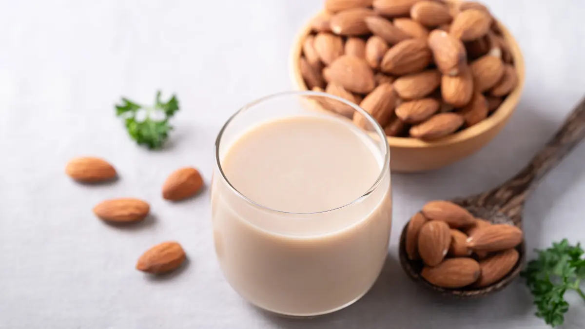 NPG-erweiterte Lizenz / Mantel, Beachten: nur redaktionelle Nutzung! Glas Mandelmilch und Mandeln auf weißem Stoffhintergrund, pflanzliche Milchalternative, laktosefrei. Download am 23.2.26 für SWP Wirtschaft. 1899037960 Foto: © nungning20/adobe.stock.com