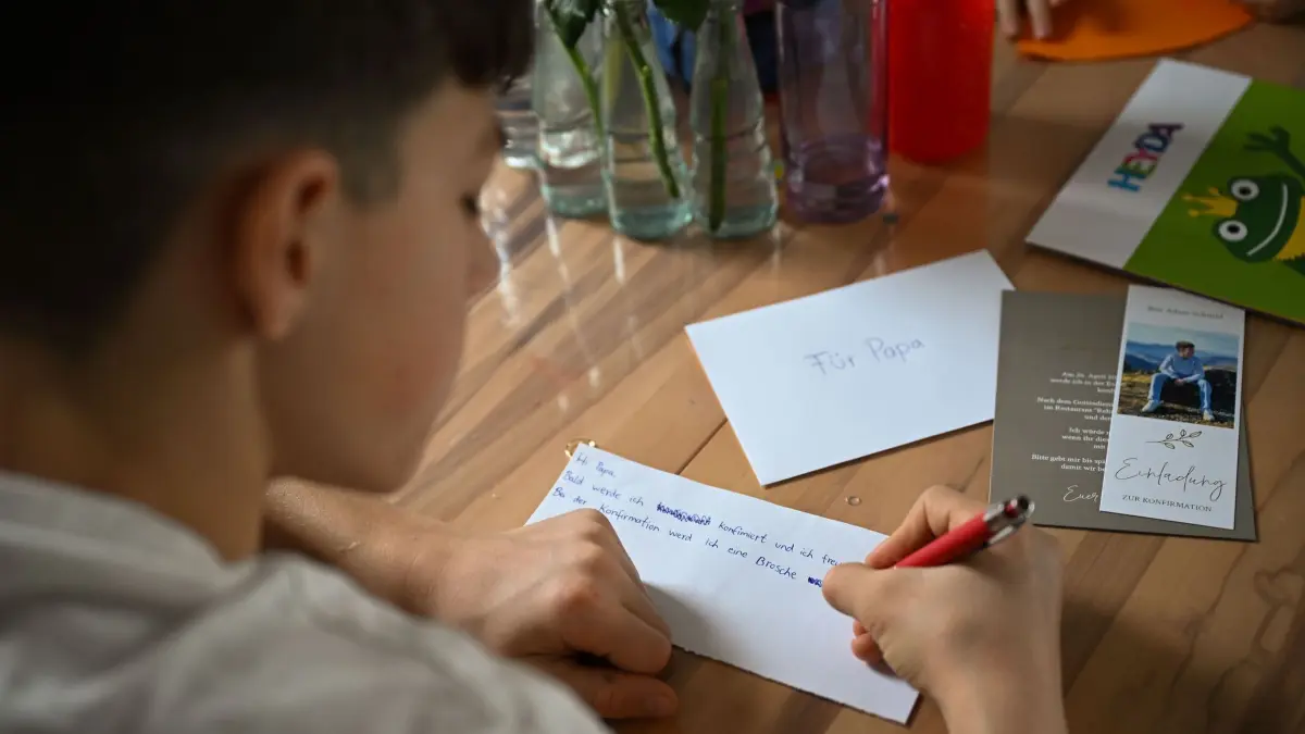 Grabsteine mit Briefschlitz: PRODUKTION - 17.02.2026, Baden-Württemberg, Bad Wildbad: Ben schreibt an einem Brief für seinen Vater. Der Familienvater starb 2023 an Krebs. Auf seinem Grab steht ein Grabstein mit Briefschlitz, in den die Familie Briefe einwerfen kann. Foto: Katharina Kausche/dpa - ACHTUNG: Nur zur redaktionellen Verwendung im Zusammenhang mit der aktuellen Berichterstattung und nur mit vollständiger Nennung des vorstehenden Credits +++ dpa-Bildfunk +++