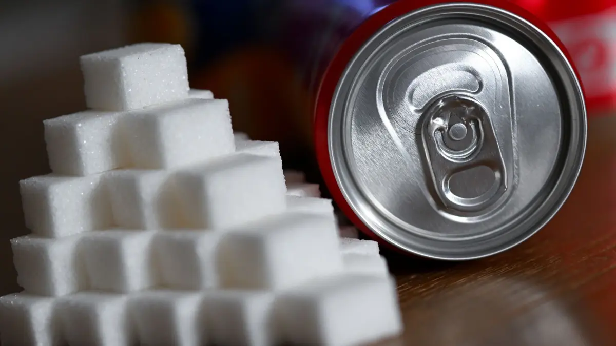 Softdrinks mit Zucker: ILLUSTRATION - 17.02.2026, Bayern, München: Eine Getränkedose mit einem Softdrink und zahlreiche Zuckerwürfel liegen auf einem Tisch. (zu dpa: «Mehrheit der Bundesbürger bewertet Zuckersteuer positiv») Foto: Sven Hoppe/dpa +++ dpa-Bildfunk +++