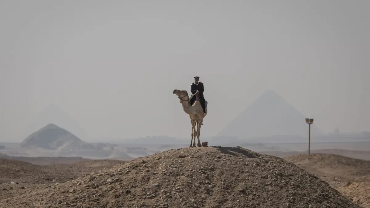 Altägyptische Stätte Sakkara: ARCHIV - 05.03.2020, Ägypten, Sakkara: Ein ägyptischer Polizist auf einem Kamel steht Wache in der Nähe der Djoser-Pyramide in Saqqara außerhalb von Kairo, hinter der sich weitere Pyramiden auf dem Gizeh-Plateau befinden. (zu dpa: «Pyramide bekritzelt: Ägyptischer Reiseführer festgenommen») Foto: Oliver Weiken/dpa +++ dpa-Bildfunk +++