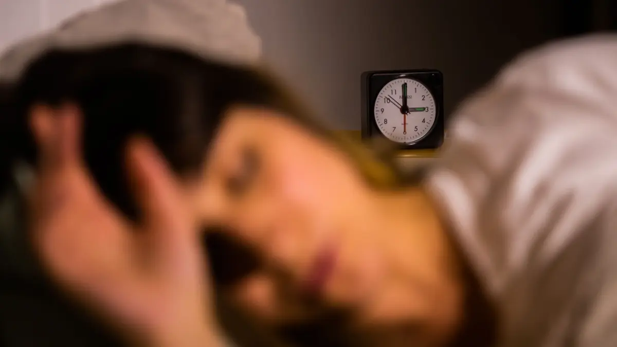 Warum träumen wir immer noch von der Schule?: ARCHIV - 27.10.2021, Berlin: Eine Frau schläft neben einem Wecker, der auf drei Uhr zeigt (gestellte Szene). Die Menschen in Frankreich schlafen immer weniger, insbesondere weil sie noch spät auf Bildschirme von Handys, Laptops oder Fernsehern schauen. (zu dpa: «Studie: Straßenlärm belastet schnell Herz und Kreislauf») Foto: Christoph Soeder/dpa +++ dpa-Bildfunk +++