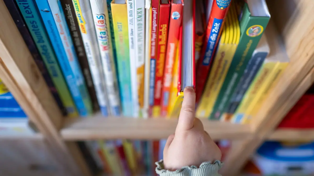Illustration - Vorlesen: ARCHIV - 26.09.2023, Sachsen, Leipzig: Ein Mädchen zieht in einem Kinderzimmer in Leipzig ein Kinderbuch aus einem Regal. (zu dpa: «Kindern aus dem Lesefrust helfen - Ehrenamtliche gesucht») Foto: Hendrik Schmidt/dpa +++ dpa-Bildfunk +++